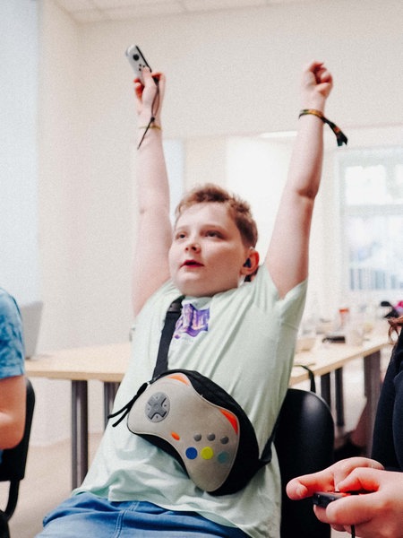 Zwei Jungen und eine Frau halten Controller in der Hand. Der Junge in der Mitte hält seine Arme nach oben in die Luft.