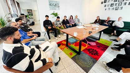 Mehrere Menschen sitzen in einem Raum auf Stühlen und Sofas