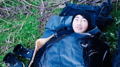Ein junger Mann liegt in einem Schlafsack im Freien