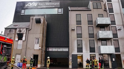 Blick auf ein graues Gebäude, davor stehen Feuerwehrleute