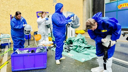 Vier Frauen in Schutzkleidug bereiten sich auf die Taubenrettung vor, indem sie ihre Atemschutzmasken reinigen.