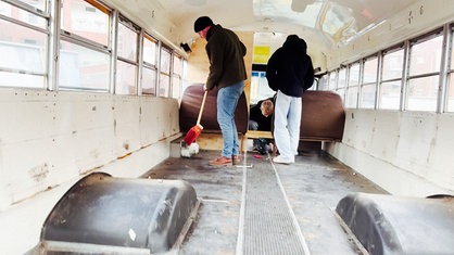 Drei Schüler stehen im leergeräumten Bus und fegen.  