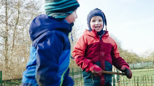 Zwei spielende Kinder in bunten Jacken, eines lacht in die Kamera