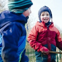 Zwei spielende Kinder in bunten Jacken, eines lacht in die Kamera