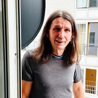 Willi Lehmann steht auf dem Balkon seiner Kölner Wohnung, lehnt am Türrahmen und lächelt.
