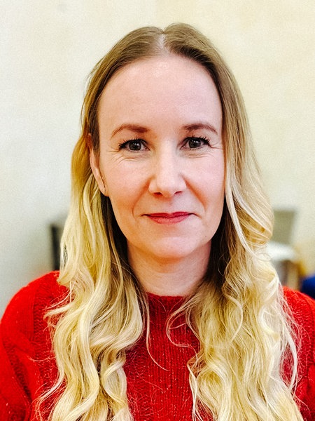 Ein Frau mit langen blonden Haaren und einem roten Pullover schaut direkt in die Kamera.