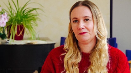 Maike Schmidt, eine Frau mit langen blonden Haaren, sitzt auf einem blauen Stuhl.