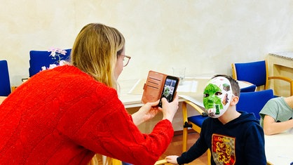 Maike Schmidt fotografiert ein Kind mit einer selbstbemalten Maske.