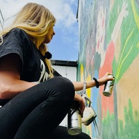 Eine junge Frau mit langen Haaren sprayt an einer Gebäudewand.
