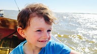 Porträt eines kleinen Jungen, der auf einem Schiff sitzend über das Meer fährt.