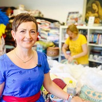 Natalya Franz steht an einem großen Nähtisch und lächelt in die Kamera.