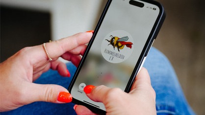 Ein Handy auf dem das Logo des Hummelhelden e. V. zu sehen ist.