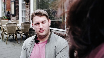 Robbin Nilles sitzt draußen in einem Café. Er schaut eine Kellnerin an.