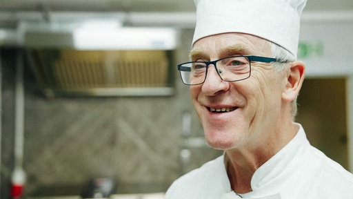 Klaus Wellmeier mit einer Kochmütze lacht in Richtung Kamera.