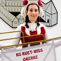 Vanessa Buch steht vor einer Wand an der eine Zeichnung einer Burg und das Wappen von Mönchengladbach hängt. In den Händen hält sie einen Banner mit der Aufschrift "KG Ruet-Wiss-Okerke". 