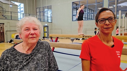 Zwei Frauen stehen in einer Sporthalle und lächeln in die Kamera.