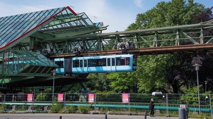 Eine hellblaue Schwebebahn fährt in Wuppertal aus einem Bahnhof