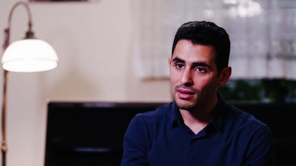 Aeham Ahmad sitzt in seiner Wohnung. Neben ihm ist eine Stehlampe.