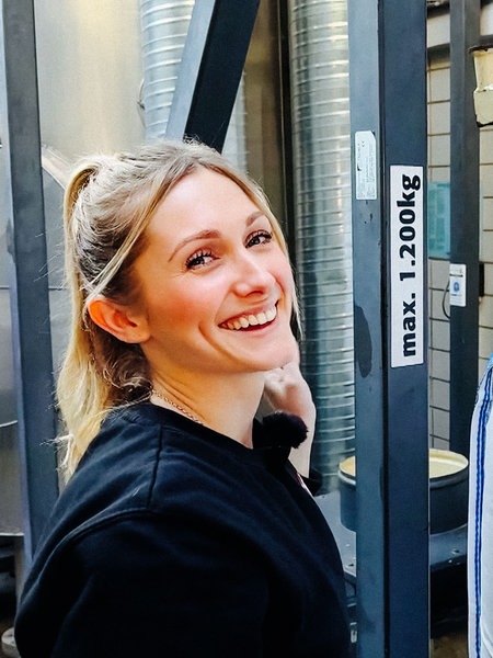 Lena Backes, eine junge Frau, steht neben einem riesigen Sack voll Malz.