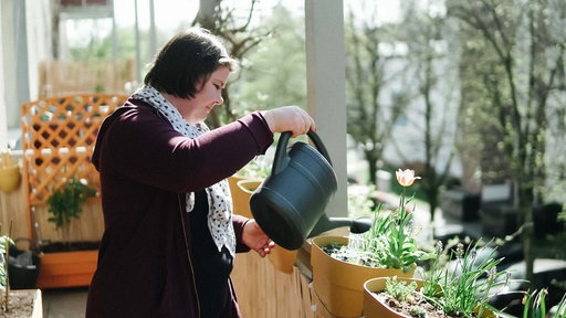 Hannah Steinfurt steht auf einem Balkon und gießt Blumen.