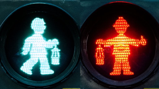 Ein rot und ein grün leuchtendes Bergmann-Ampelmännchen mit Helm auf dem Kopf und Lampe in der Hand.