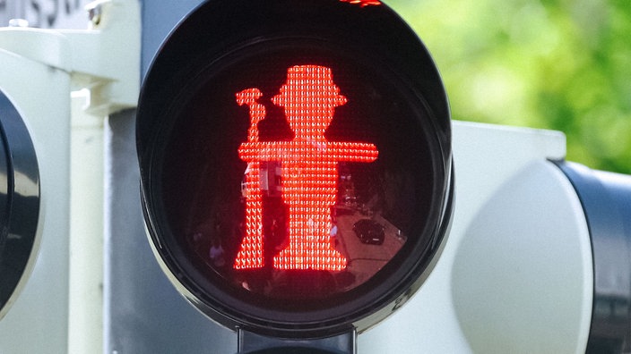 Ein rotes Ampelmännchen an einer Ampel hält ein Gewehr und trägt einen Schützenhut.