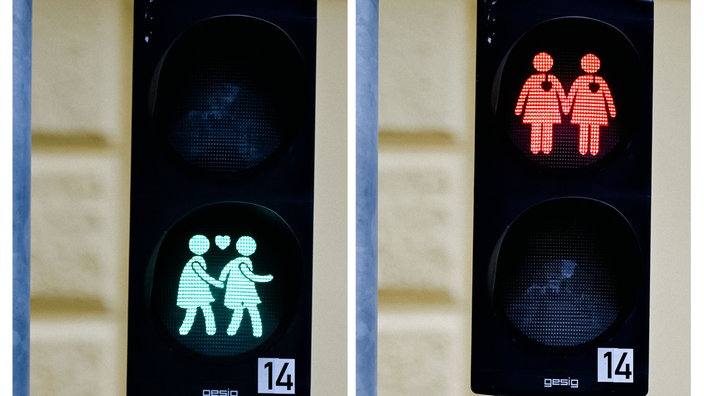 Zwei Ampeln zeigen gleichgeschlechtliche Paare, die Händchen halten. Das Paar, das grün leuchtet, läuft. Das rot leuchtende Paar steht.