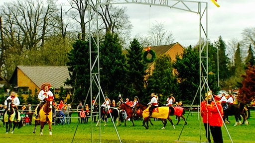 Reiter mit Pferden reiten unter einem Gestell, an dem ein Kranz hängt