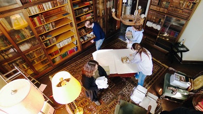 Die Bibliothek von Schloss Bodelschwingh von oben mit Regalen aus dunklem Holz und dem Team, das die Bücher ausräumt.
