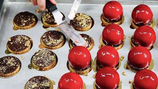 Rote Pralinen in Kugelform und flache, mit Schokolade verzierte Pralinen liegen auf einem Blech.