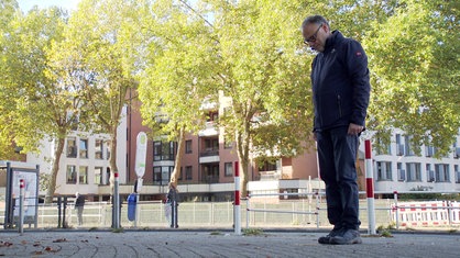 Alfred Brechner steht auf dem Bürgersteig an der Ringstraße und schaut nach unten auf die Stolpersteine seiner Familie.
