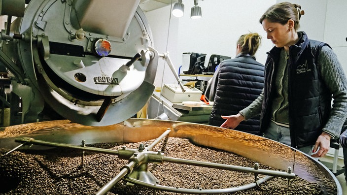 Gina Vogeler steht an der Röstmaschine schaut auf die gerösteten Kaffeebohnen.