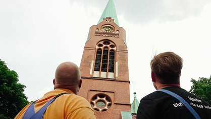 Zwei Männer blicken an einem Kirchturm hoch