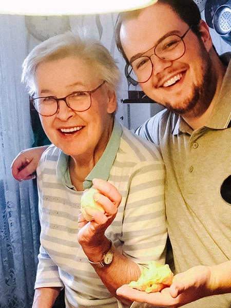 Melvin Flor legt seinen Arm um seine Großmutter. Sie stehen in der Küche und lachen.