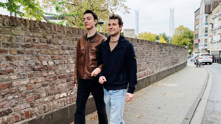Arno Groß und Marvin Knappmeier laufen auf einem Bürgersteig. Sie haben sich beieinander eingehakt.