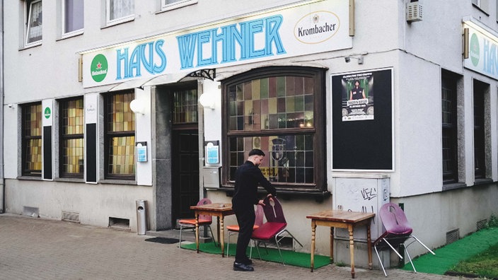 Ein altes Gebäude von außen mit der Aufschrift "Haus Wehner". Davor Jendi Mahmud, der einen Stuhl umstellt.