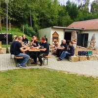 Mehrere Menschen sitzen auf Bänken und Steinen und essen gemeinsam.