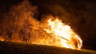 Ein Holzrad, das mit brennendem Stroh umspannt ist, rollt in Lügde einen Abhang herunter