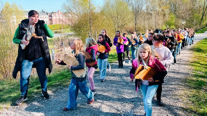 Viele Kinder und eine Frau laufen mit ihren Räppeln in den Händen einen Weg entlang.