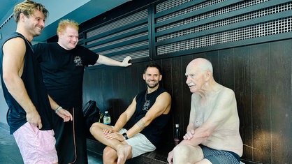 Harald Peters, Schwimmtrainer Tobias Krämer und die Gründer der Schwimmschule auf einer Bank neben dem Schwimmbecken