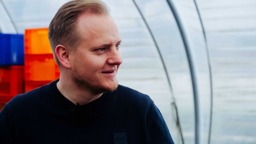 Mann mit lichtem blondem Haar und schwarzem T-Shirt, Oberkörper samt Blick nach rechts geneigt