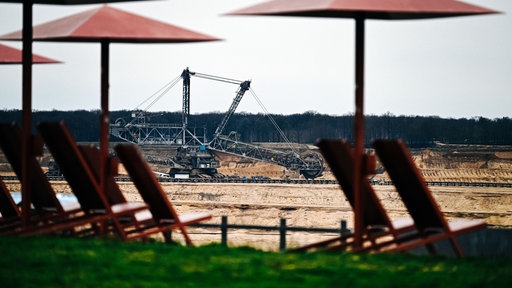 Am Rande des Tagebaus Hambach stehen Stühle mit Sonnenschirmen.