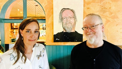 Der ehemalige Wirt Erich Winers steht mit der neuen Besitzerin der Kastanie am Hax, Julia Söhngen, vor einem gemalten Portrait von ihm