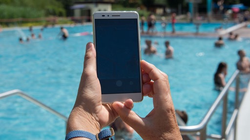Ein Smartphone, dass im Freibad auf das Schwimmbecken gerichtet wird