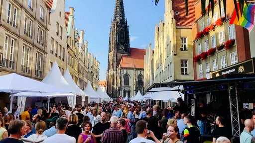 Menschen und weiße Pavillons auf einer Straße, im Hintergrund ist eine Kirche zu sehen