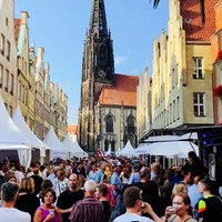 Menschen und weiße Pavillons auf einer Straße, im Hintergrund ist eine Kirche zu sehen