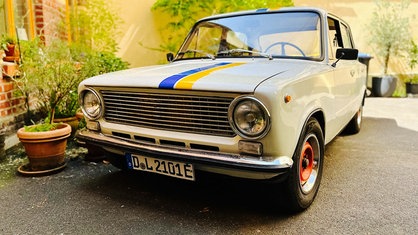 Der Lada von Andrea Giacin steht neben mehreren Pflanzentöpfen in einem Innenhof. Das Auto ist mattweiß und hat blaue und gelbe Streifen auf der Motorhaube. 