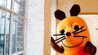 Das Maskottchen der ,,Sendung mt der Maus" steht neben einem Fenster
