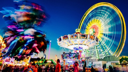 Ein Rummelplatz bei Nacht mit beleuchtetem Riesenrad und Kettenflieger