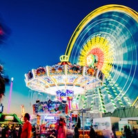Ein Rummelplatz bei Nacht mit beleuchtetem Riesenrad und Kettenflieger